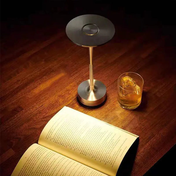 The Tower Table lamp on a wood desk with a drinking glass and book. 